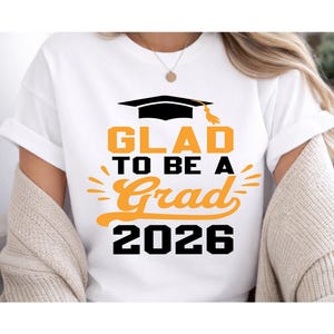 A white t-shirt with a graphic design that says "GLAD TO BE A GRAD 2026" printed on it.