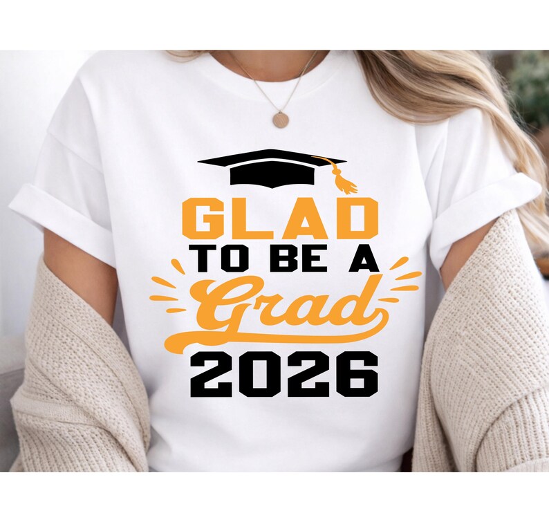 A white t-shirt with a graphic design that says "GLAD TO BE A GRAD 2026" printed on it.
