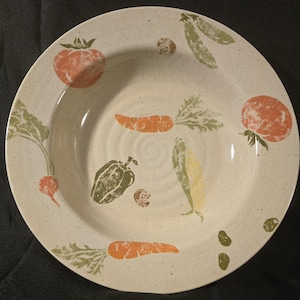 May include: A white ceramic soup bowl with a vegetable design. The bowl features green, orange, and red vegetables, including carrots, peppers, and tomatoes.