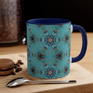 May include: A blue and white ceramic coffee mug with a colorful geometric pattern. The mug has a blue rim and handle.