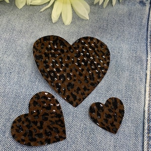 May include: Three brown heart-shaped patches with a leopard print design. The patches are on a blue denim background.