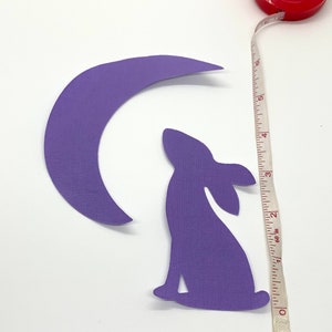 May include: Purple paper cutouts of a crescent moon and a rabbit. A red tape measure shows the length of the rabbit cutout is approximately 3 inches. The tape measure is marked in inches and has the text "Fusion Beads".