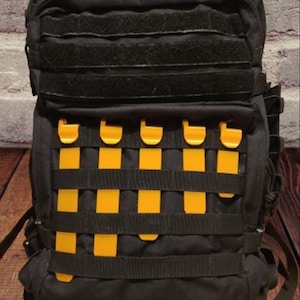 May include: Black tactical backpack with yellow straps and buckles. The backpack has a large main compartment and several smaller pockets.