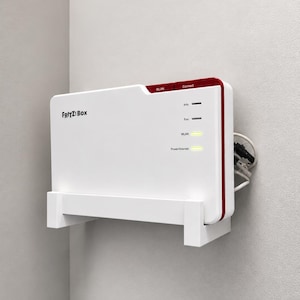 Puede incluir: Un router FRITZ!Box blanco y rojo montado en una pared mediante un soporte de plástico blanco. El dispositivo presenta el texto FRITZ!Box en el frente, con etiquetas para WLAN y Connect, y luces de estado amarillas encendidas para WLAN.