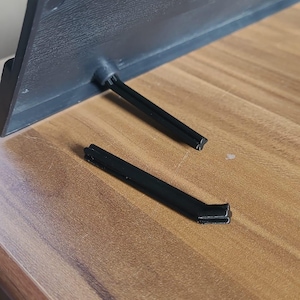 Könnte beinhalten: Zwei schwarze Plastik-Ständer für ein Tablet oder einen Laptop. Die Ständer sind vom Gerät getrennt und liegen auf einer Holzoberfläche.