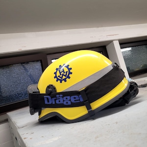 May include: A yellow safety helmet with a black strap and a blue and white logo that says "Dräger".