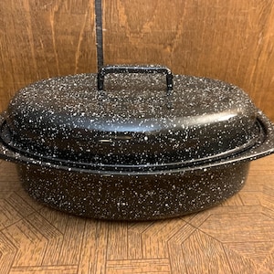 以下が含まれることがあります： 蓋とハンドルが付いた、黒い斑点のあるローストパン。 楕円形のパンは木製の表面に置かれています。 蓋には持ち上げやすいようにハンドルが付いています。 このパンは調理とベーキング用に設計されています。