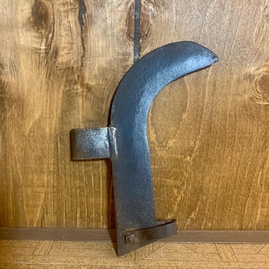 May include: A curved, rusty metal tool with a leather strap. The tool has a sharp edge and a handle with a metal loop.