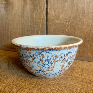 May include: A white ceramic mixing bowl with a speckled brown and blue glaze. The bowl is round and has a slightly flared rim.