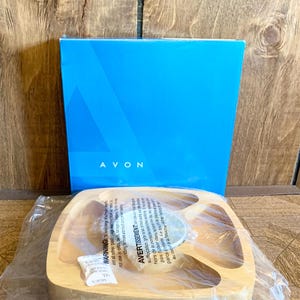 May include: A wooden serving tray with four compartments and a central dip bowl, packaged in plastic. A blue box with the word "AVON" is in the background. The tray is light brown.