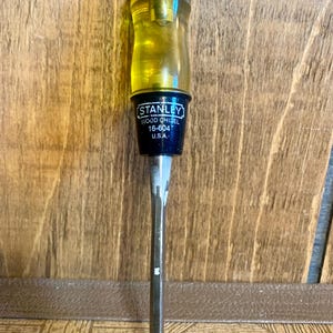 May include: A yellow and black Stanley wood chisel with a wooden handle. The chisel is labeled "Stanley Wood Chisel 16-604 U.S.A."