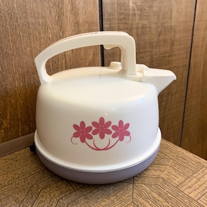 May include: Cream-colored electric kettle with a white handle and spout. The kettle features a pink floral design on the front and a gray base. The handle is arched and the spout is on the right side.