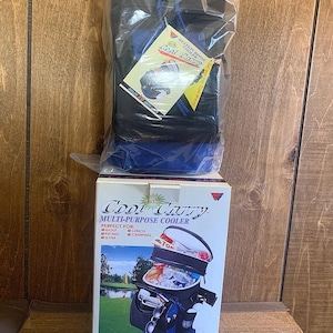 Peut inclure: Un sac isotherme multi-usages Deluxe Cool Carry noir et bleu, parfait pour le golf, le déjeuner, le pique-nique, le camping et la salle de sport. Le sac est présenté dans son emballage d'origine, avec une étiquette. L'emballage montre également une photo du sac en cours d'utilisation.