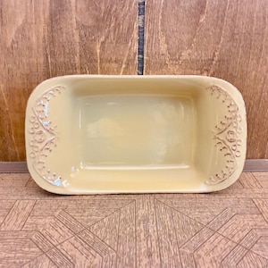 Puede incluir: Una fuente de horno rectangular de cerámica en color crema claro. La fuente presenta esquinas redondeadas y patrones florales en relieve en los lados interiores izquierdo y derecho, con un acabado liso y brillante en toda la superficie interior.