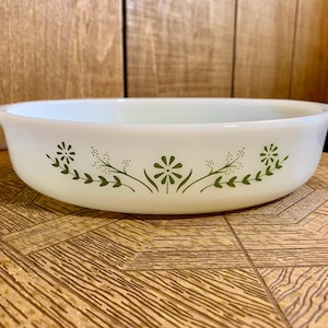 Puede incluir: Fuente ovalada blanca con diseño floral verde. La fuente tiene dos asas y un patrón decorativo de flores y hojas estilizadas. La fuente está hecha de un material duradero y es adecuada para hornear y servir.