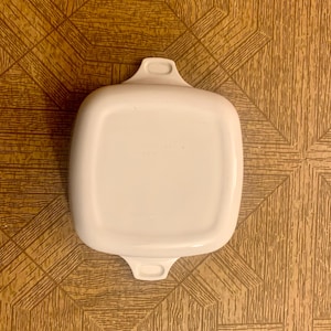 May include: White square baking dish with two handles. The dish is made of ceramic and has a smooth, glossy finish.
