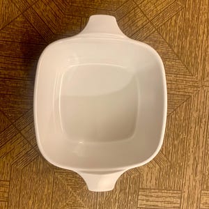 May include: White ceramic baking dish with two handles. The dish is square shaped and has a smooth, glossy finish.
