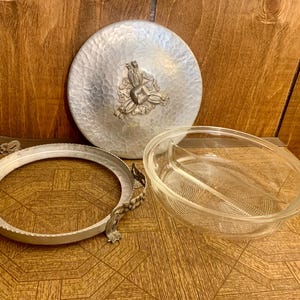 Könnte beinhalten: Eine silberne Servierplatte mit einem gehämmerten Metalldesign und einem floralen Akzent. Die Platte hat einen klaren Glaseinsatz mit zwei Abschnitten.