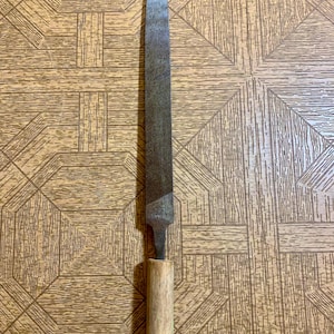 May include: A long, metal file with a wooden handle. The file is rusty and has a green paint mark on the handle.