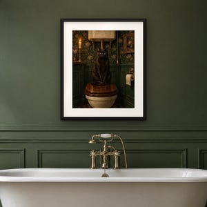 May include: A framed wall art print featuring a black cat sitting on a wooden toilet seat in a dimly lit bathroom. The scene includes a lit candle, floral wallpaper, and a toilet paper roll, all enclosed within a black frame with a white mat.