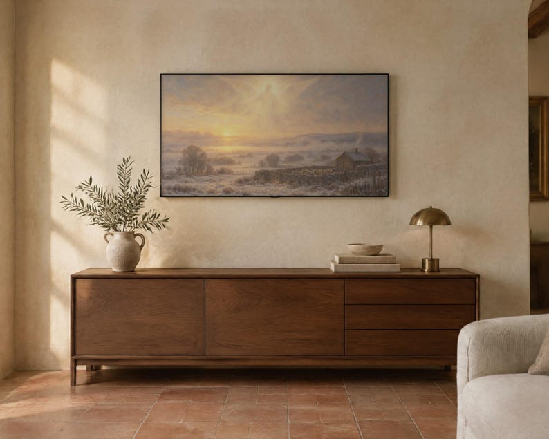 May include: A rectangular landscape painting featuring a misty sunrise over a rural field with a small house, stone walls, and a faint winged figure in the sky, displayed in a thin black frame above a long wooden sideboard with drawers.