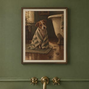 May include: A framed wall art print depicting a brown and white terrier dog wrapped in a striped towel, sitting on a rug in a bathroom next to a clawfoot tub. Dark paw prints are visible on the wooden floorboards leading away from the dog.