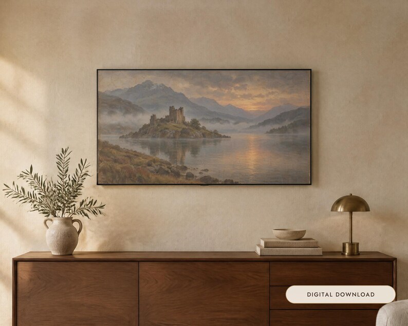 May include: A rectangular landscape painting in a thin black frame depicting a stone castle on a small island in a lake surrounded by misty mountains at sunset. The artwork features soft golden light reflecting on the water and cloudy skies.