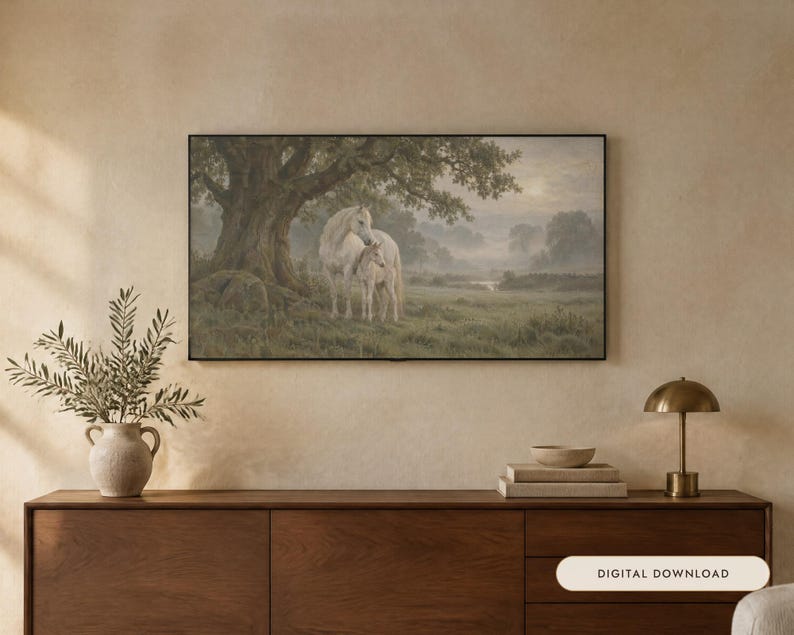 May include: A rectangular wall art print in a black frame depicting a white horse and foal standing under a large tree in a misty, green meadow. The artwork features a soft, muted color palette with a hazy sunlit sky in the background.