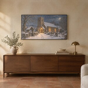 Puede incluir: Una impresi&oacute;n de arte mural rectangular que representa una iglesia de piedra en un paisaje invernal nevado por la noche, con ventanas de brillo c&aacute;lido, un camino cubierto de nieve y &aacute;rboles desnudos bajo un cielo iluminado por la luna, enmarcada en un borde negro fino.