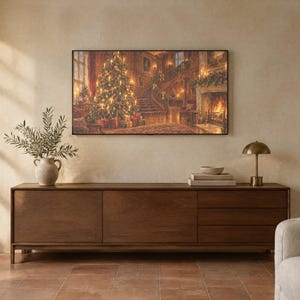 May include: A long, rectangular wooden sideboard with three drawers and two cabinet doors. On top sits a ceramic vase with green branches, a stack of books, and a small brass lamp. A large framed print of a Christmas scene hangs above.