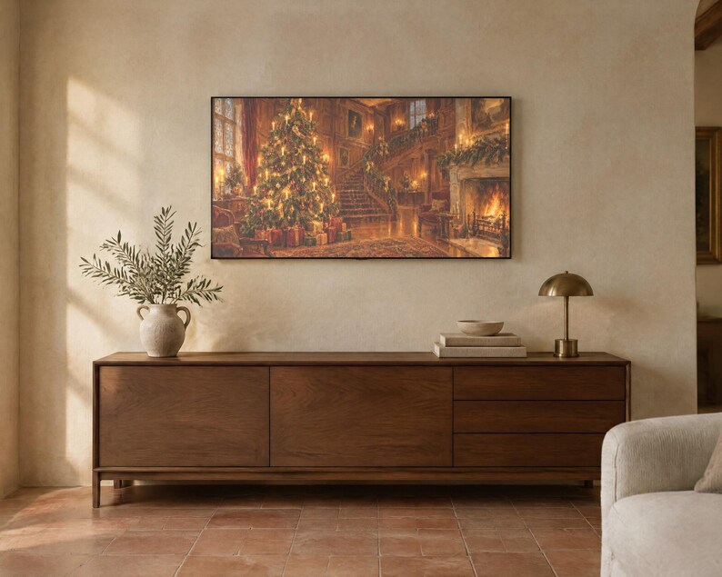May include: A long, rectangular wooden sideboard with three drawers and two cabinet doors. On top sits a ceramic vase with green branches, a stack of books, and a small brass lamp. A large framed print of a Christmas scene hangs above.