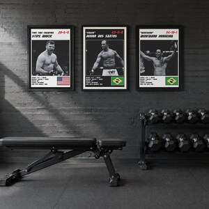 May include: Three framed black and white posters featuring MMA fighters Stipe Miocic, Junior dos Santos, and Minotauro Nogueira. Each poster displays the fighter's name, record, physical stats, and a national flag in the bottom corner.