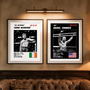 May include: Two framed posters featuring black and white photographs of UFC fighters Conor McGregor and Daniel Cormier. Each print includes the fighter's name, nickname, record, physical stats in imperial units, and a national flag.