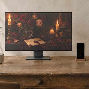 May include: A computer monitor displaying a still life painting of red roses, lit candles, and a sealed envelope on a dark surface. The monitor sits on a wooden desk next to a ceramic mug, a smartphone on a wooden stand, and a notebook.