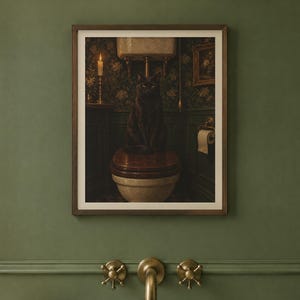 May include: A framed wall art print featuring a black cat sitting on a toilet in a dimly lit bathroom with dark floral wallpaper, a lit candle on a shelf, and a roll of toilet paper hanging on the wall next to the toilet fixture.