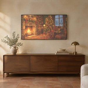 May include: A long, rectangular dark wood sideboard with two cabinet doors and three drawers. On top sits a ceramic vase with green branches, a stack of books, and a small brass lamp. A large framed print of a cozy fireplace scene hangs above.