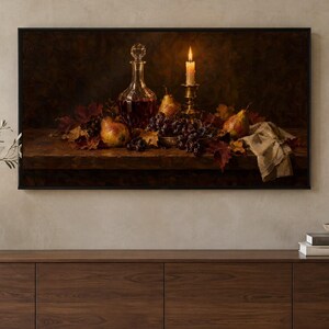 May include: A framed rectangular wall art print depicting a dark still life scene with a glass decanter, a lit candle in a brass holder, pears, and dark grapes resting on a wooden surface amidst scattered autumn leaves and a cloth.