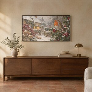 May include: A rectangular wall art print featuring a winter scene with a robin perched on a holly branch in the foreground and a snow-covered cottage in the background. The artwork is framed in a thin black border and displayed on a wall.