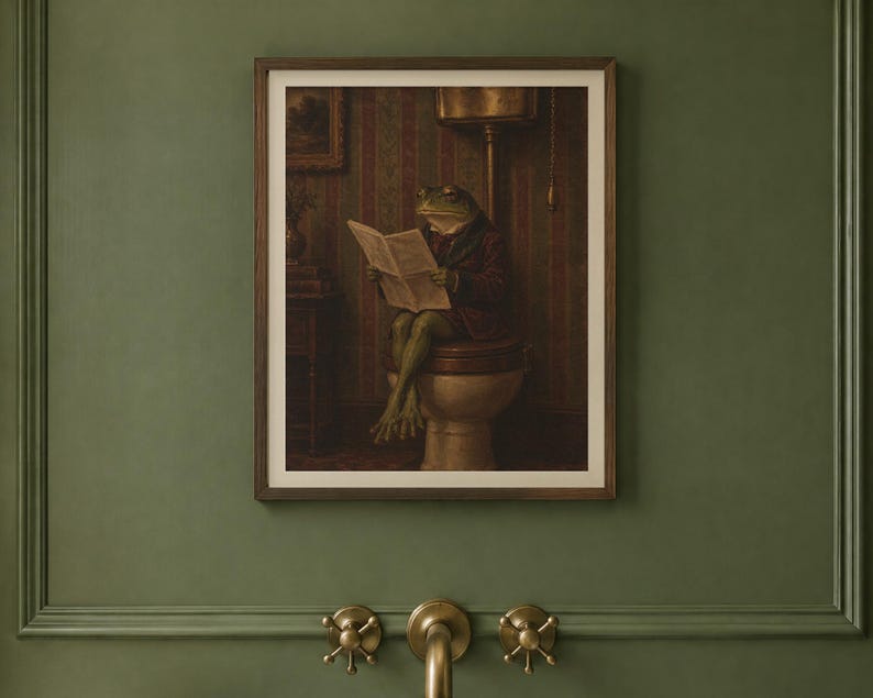 May include: A framed wall art print featuring an anthropomorphic frog wearing a dark jacket, sitting on a toilet while reading a newspaper. The scene is set in a dimly lit room with striped wallpaper, presented in a dark wood frame.