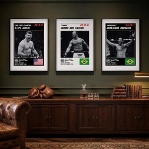 May include: Three framed posters featuring black and white photographs of MMA fighters Stipe Miocic, Junior Dos Santos, and Minotauro Nogueira. Each print includes the fighter's name, record, statistics, and a national flag in a white border.
