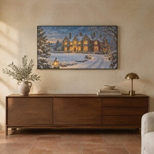 May include: A rectangular wall art print depicting a large stone manor house covered in snow at twilight. The scene features a winding driveway, glowing outdoor lanterns, and snow-dusted trees under a soft, cloudy sky with warm interior lighting.