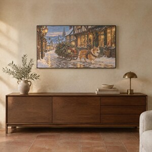 May include: A rectangular wall art print depicting a snowy village street scene with a corgi pulling a small wooden sled loaded with a Christmas tree and gifts, displayed above a long, dark brown wooden sideboard with three drawers.