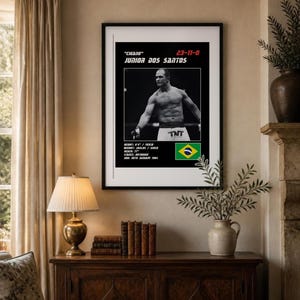 Peut inclure: Une affiche encadr&eacute;e avec une photo en noir et blanc de Junior Dos Santos, le texte "Cigano" 23-11-0, taille 193cm, poids 120kg, allonge 77", posture orthodoxe, date de naissance 30 janvier 1984 et le drapeau du Br&eacute;sil.