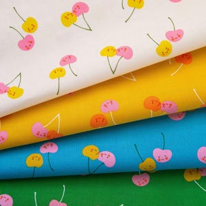 May include: Close-up of four fabric samples with a repeating cherry pattern. The cherries have smiling faces and are in shades of pink and yellow. The fabric colours are white, yellow, blue, and green.