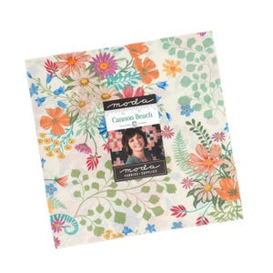 May include: A square fabric bundle with a floral pattern in orange, pink, blue, and green. The fabric is labeled "Cannon Beach" by Moda Fabrics. The bundle features a variety of flowers and foliage on a cream background.