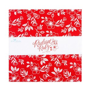 May include: A stack of red fabric squares with a white floral pattern. A white band across the center reads "Radiant Ruby" by Dani Mogstad. The fabric is suitable for quilting and other craft projects.