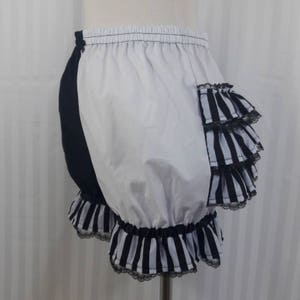 Pode incluir: Bloomers de algod&atilde;o listradas em preto e branco com acabamento de renda preta e um detalhe de babado listrado em preto e branco no lado.