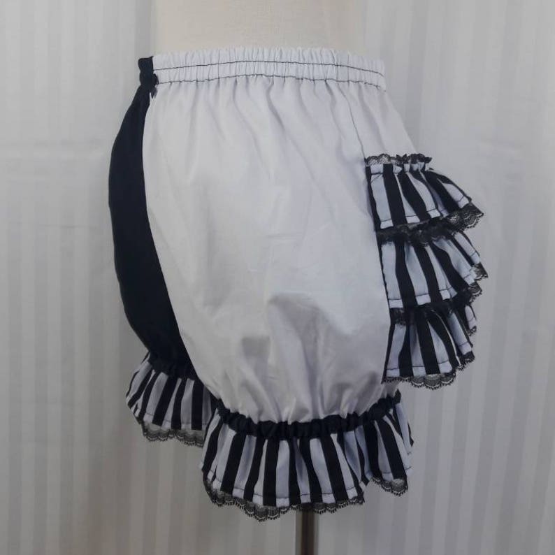 Pode incluir: Bloomers de algod&atilde;o listradas em preto e branco com acabamento de renda preta e um detalhe de babado listrado em preto e branco no lado.