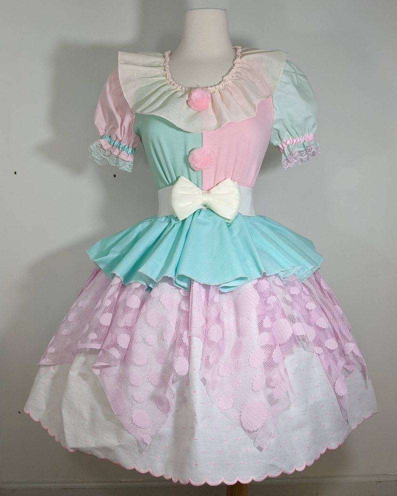 May include: A pastel-colored dress with a ruffled collar, a pink and green bodice, and a layered skirt with pink polka dots. The dress has a white sash with a large bow.