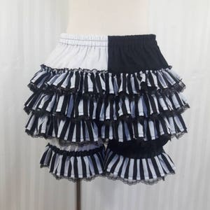 Pode incluir: Shorts de babados listrados em preto e branco com acabamento em renda preto e branco. Os shorts s&atilde;o divididos ao meio, com um lado branco e o outro preto.